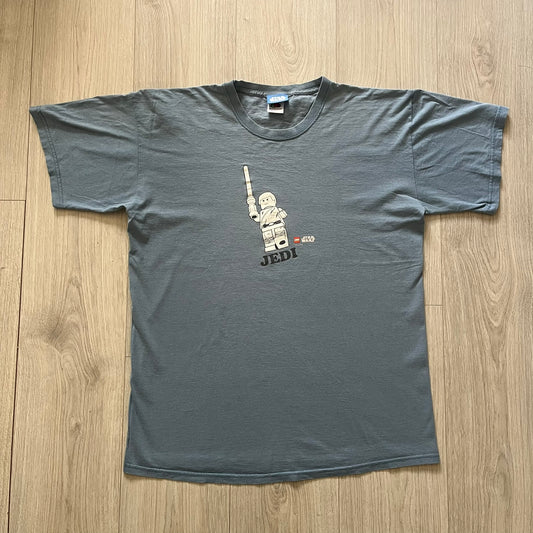Vintage Lego Star Wars Jedi tee from 2008 in light blue. Showcases a clean white Lego Skywalker graphic with lightsaber and bold “Jedi” lettering underneath. Officially licensed and made on a soft Fruit of the Loom blank.