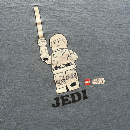 Vintage Lego Star Wars Jedi tee from 2008 in light blue. Showcases a clean white Lego Skywalker graphic with lightsaber and bold “Jedi” lettering underneath. Officially licensed and made on a soft Fruit of the Loom blank.