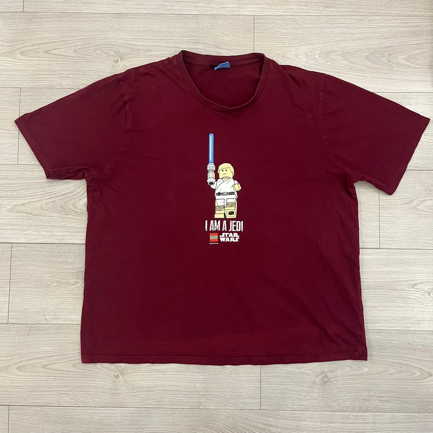 This Lego Star Wars 2008 Jedi Tee (XXXL) in burgundy showcases Luke Skywalker wielding a blue lightsaber with a 'cracked' “I Am a Jedi” text. Officially licensed by Lego Star Wars, the tee includes authentic 2008 branding under the Luke minifigure graphic.