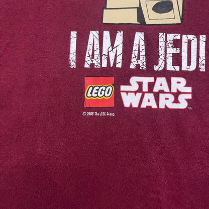 This Lego Star Wars 2008 Jedi Tee (XXXL) in burgundy showcases Luke Skywalker wielding a blue lightsaber with a 'cracked' “I Am a Jedi” text. Officially licensed by Lego Star Wars, the tee includes authentic 2008 branding under the Luke minifigure graphic.