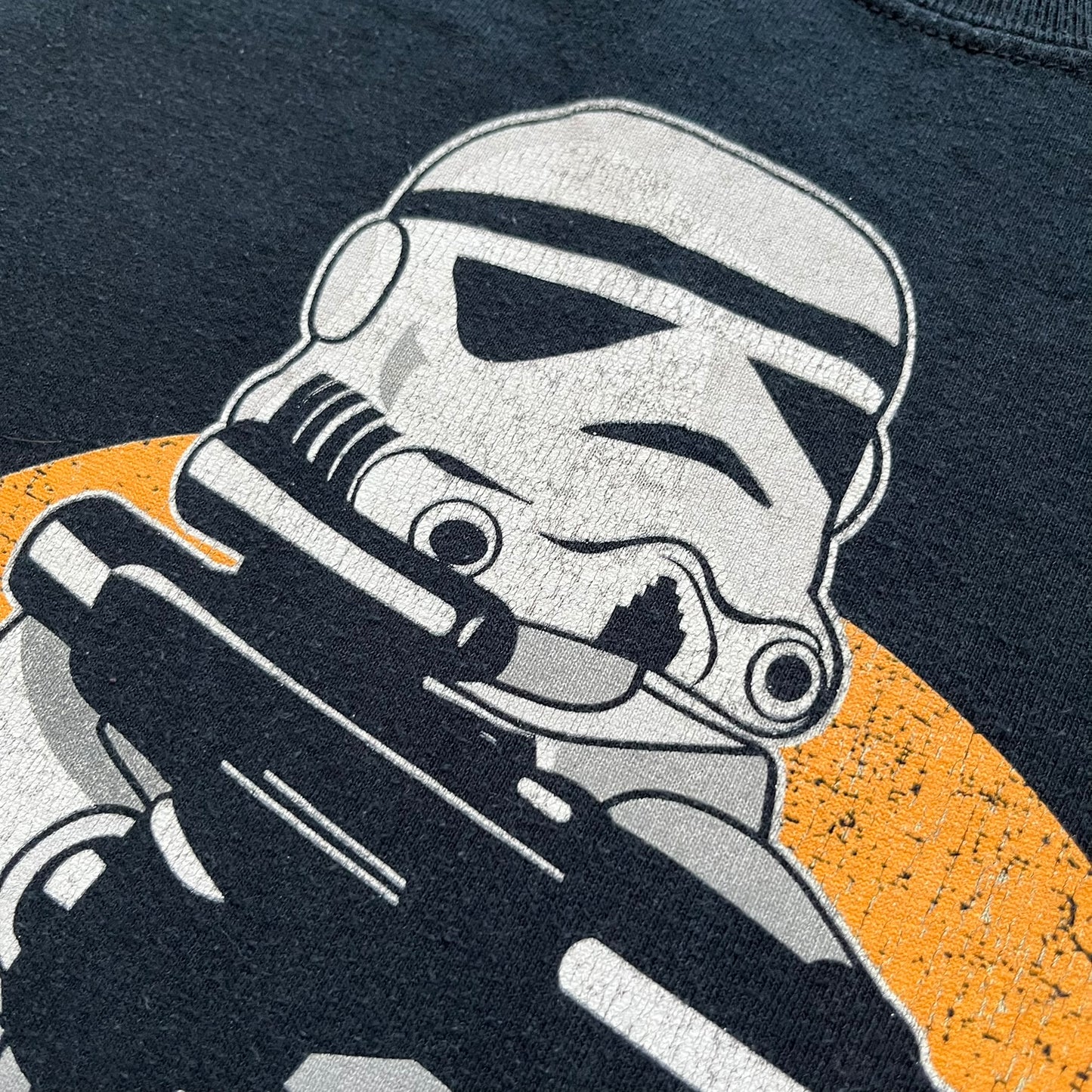 Lego Star Wars 2010 Stormtrooper Tee is a black T-shirt featuring a front graphic of a Lego Stormtrooper holding a blaster against an orange background. Below the graphic is the text “These aren’t the droids we’re looking for…” along with the Lego Star Wars logo and small 2010 licensing print.