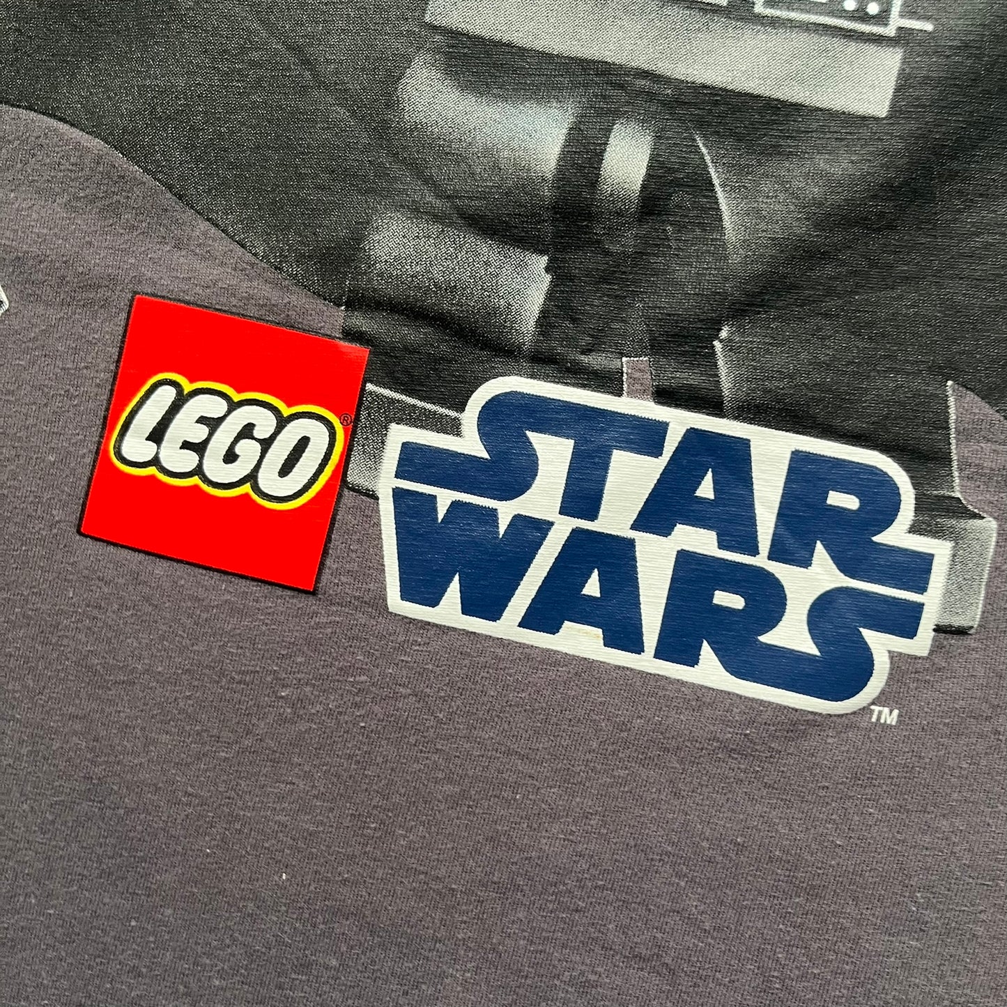 LEGO Star Wars 2012 Darth Vader Tee is a gray-brown cotton T-shirt featuring a large front graphic of Darth Vader holding a red lightsaber in a triumphant pose. The design includes three small TIE fighters flying beside him, with the LEGO Star Wars logo printed underneath. The shirt includes a 2012 licensed neck tag and official Star Wars branding.
