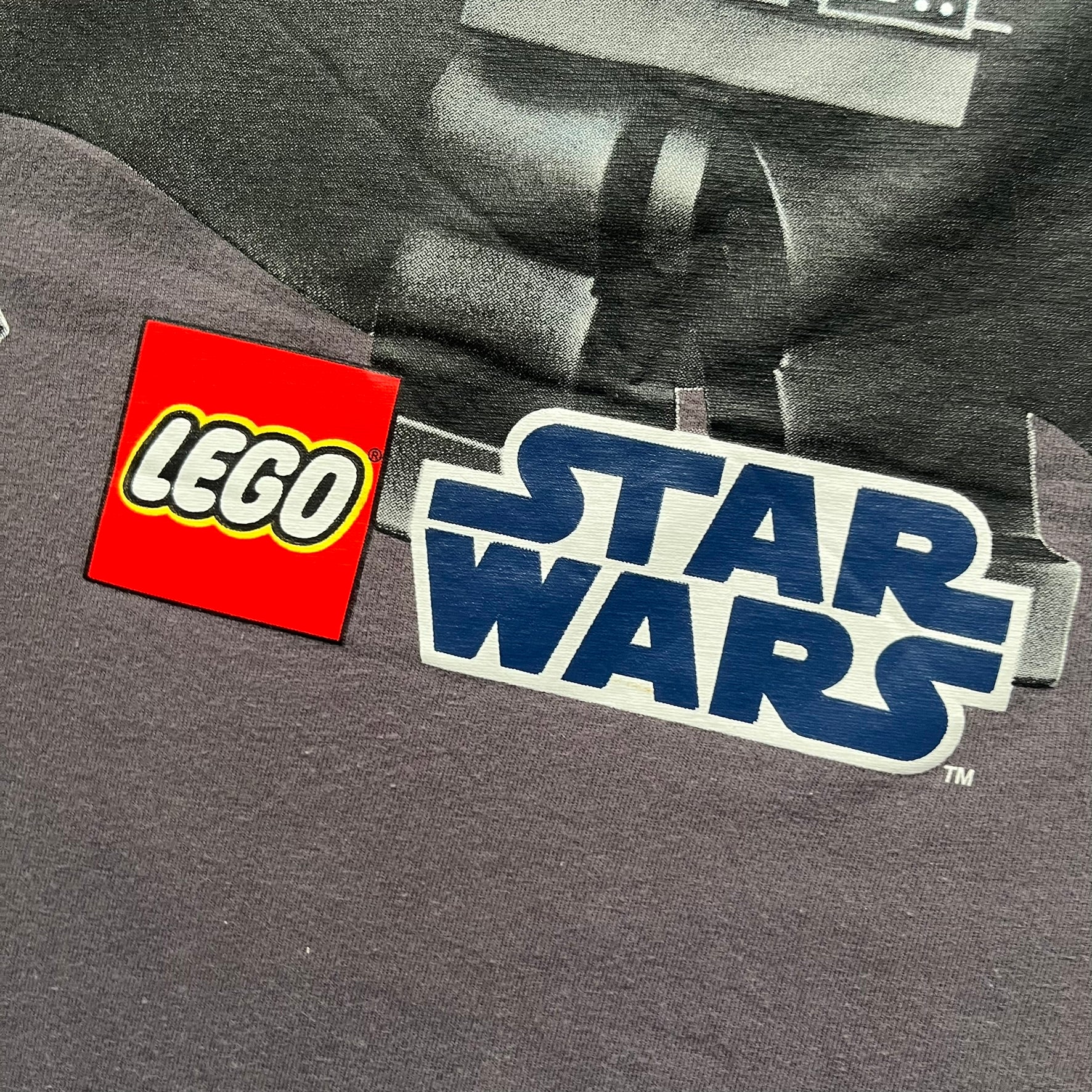 LEGO Star Wars 2012 Darth Vader Tee is a gray-brown cotton T-shirt featuring a large front graphic of Darth Vader holding a red lightsaber in a triumphant pose. The design includes three small TIE fighters flying beside him, with the LEGO Star Wars logo printed underneath. The shirt includes a 2012 licensed neck tag and official Star Wars branding.