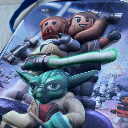 Lego Star Wars III: The Clone Wars Shoulder Bag is a blue shoulder bag featuring a raised 3D front graphic panel (not printed) with Lego Star Wars artwork. The design shows Obi-Wan Kenobi, Anakin Skywalker, and Yoda with lightsabers on a battlefield scene, with clone troopers, Ahsoka Tano, and General Grievous in the background.