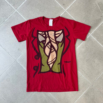Lego The Hobbit 2014 Press Kit Red Tee features a red T-shirt with a full-front graphic designed to resemble Bilbo Baggins’ outfit in LEGO form, including a green undershirt, beige tie, and dark details. The upper back has a LEGO The Hobbit logo with 2014 licensing text. Originally included as part of a press kit with additional items.