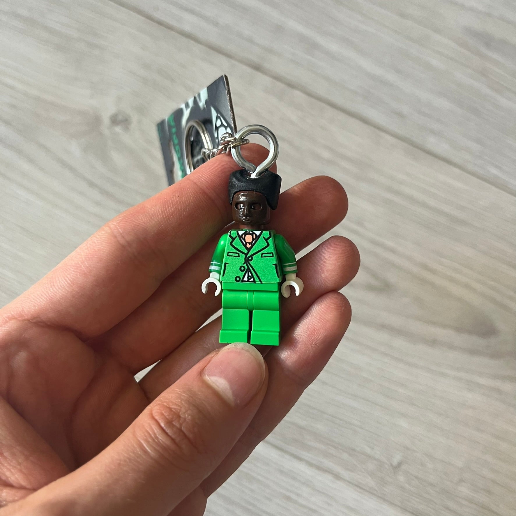 Lego x Tyler, the Creator “Brickakopia” keychain featuring a custom Lego figure of Tyler in a green suit. The figure is attached to a Lego-style recreation of the 2024 Chromakopia album cover, reimagined in brick graphics. A playful and creative collectible that merges music culture with fan-made Lego artistry, made by TheCanvasDon.