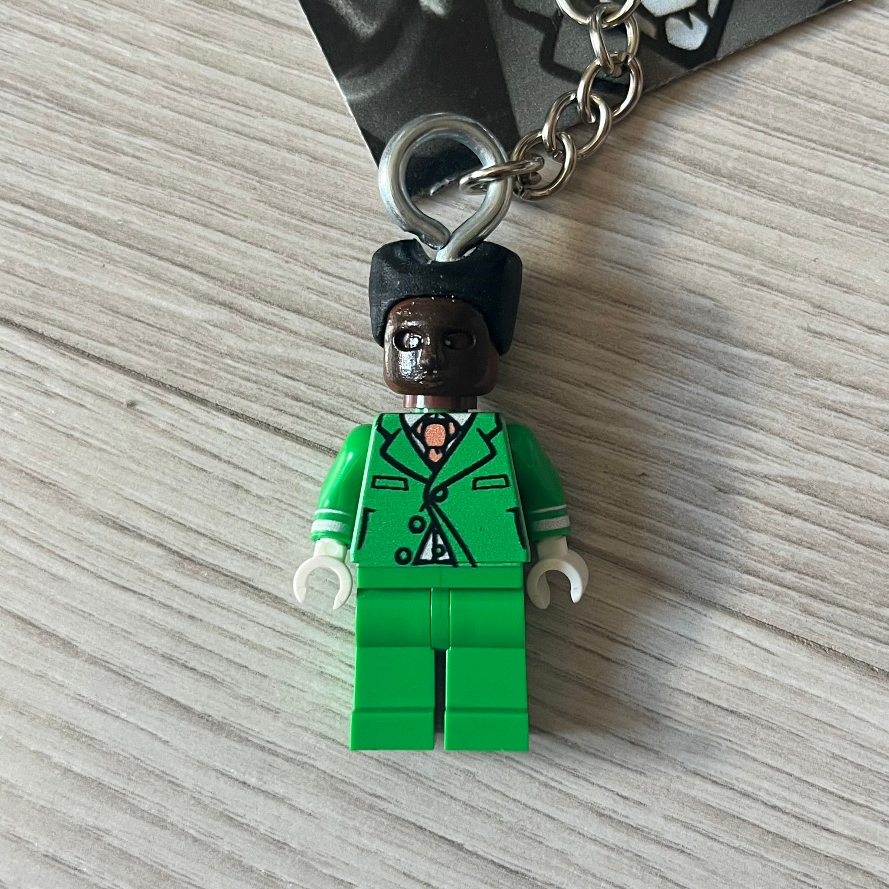 Lego x Tyler, the Creator “Brickakopia” keychain featuring a custom Lego figure of Tyler in a green suit. The figure is attached to a Lego-style recreation of the 2024 Chromakopia album cover, reimagined in brick graphics. A playful and creative collectible that merges music culture with fan-made Lego artistry, made by TheCanvasDon.
