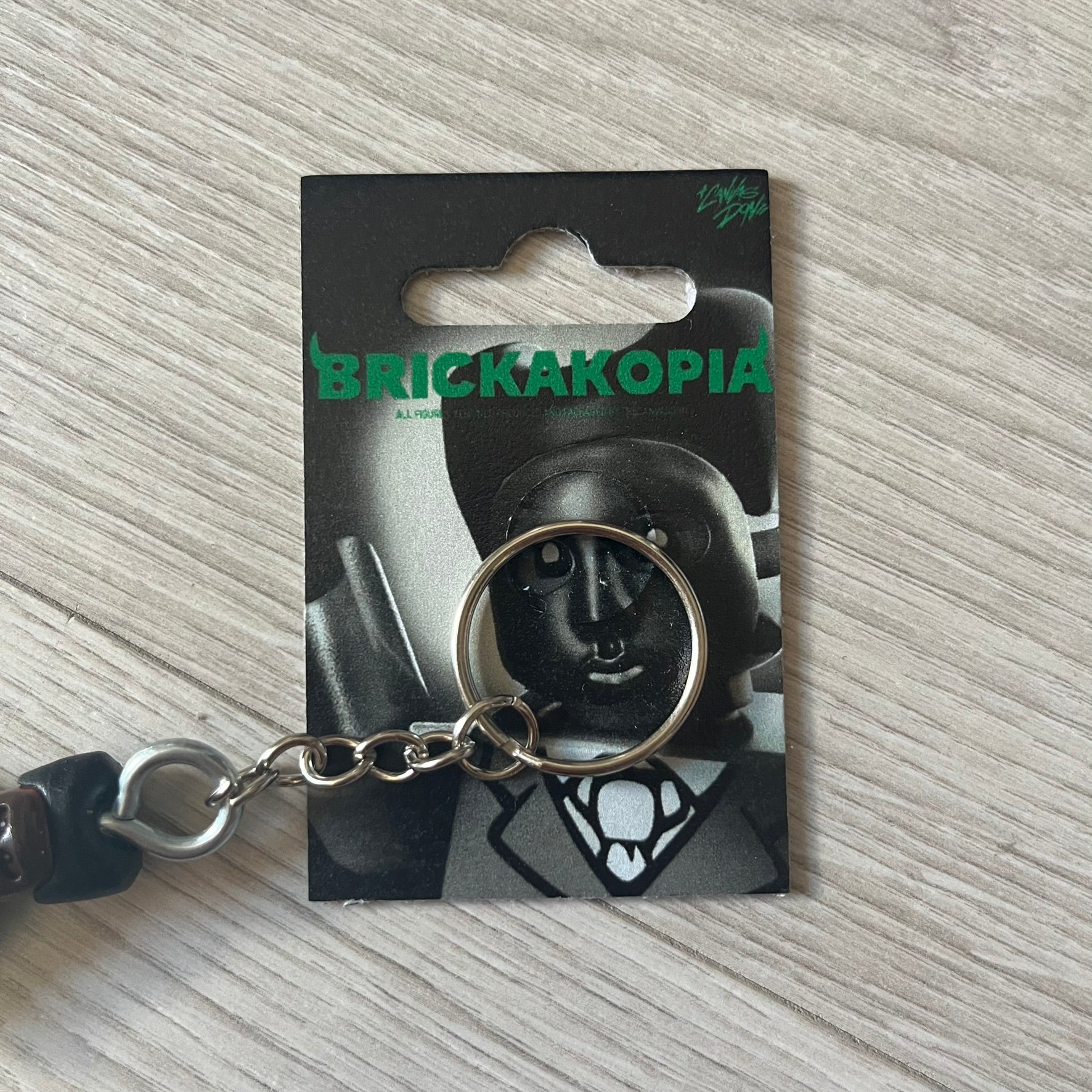 Lego x Tyler, the Creator “Brickakopia” keychain featuring a custom Lego figure of Tyler in a green suit. The figure is attached to a Lego-style recreation of the 2024 Chromakopia album cover, reimagined in brick graphics. A playful and creative collectible that merges music culture with fan-made Lego artistry, made by TheCanvasDon.