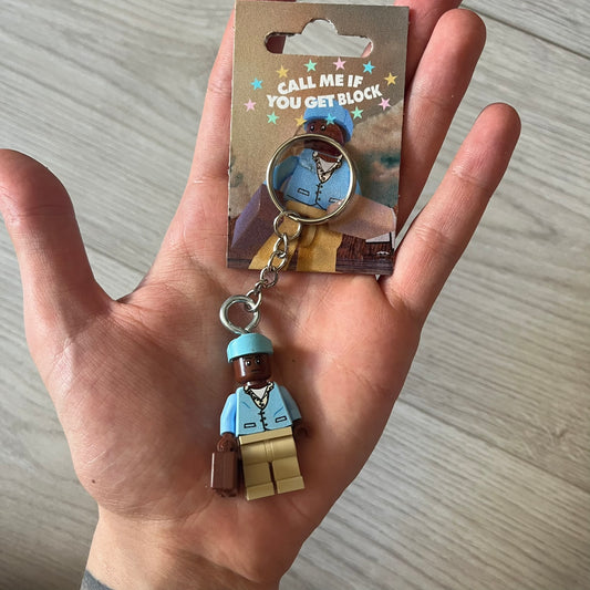 Lego x Tyler, the Creator “Call Me If You Get Block” keychain featuring a custom Lego figure of Tyler in a blue jacket with matching ushanka and suitcase. The figure is mounted on a Lego-style recreation of the 2021 Call Me If You Get Lost album cover, reimagined entirely in brick graphics. A unique collectible that blends music culture with playful Lego-inspired design, made by TheCanvasDon.