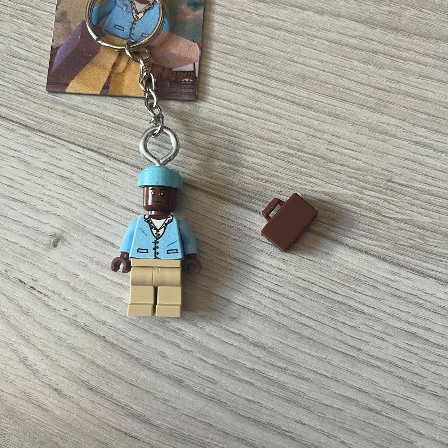Lego x Tyler, the Creator “Call Me If You Get Block” keychain featuring a custom Lego figure of Tyler in a blue jacket with matching ushanka and suitcase. The figure is mounted on a Lego-style recreation of the 2021 Call Me If You Get Lost album cover, reimagined entirely in brick graphics. A unique collectible that blends music culture with playful Lego-inspired design, made by TheCanvasDon.