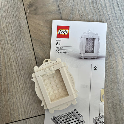 LEGO White Frame Make and Take Build is a limited promotional LEGO set distributed as an exclusive “make & take” event and not available for retail purchase. The model features a fully white 3D frame styled like a picture frame, designed for use as a photo holder. The back includes a hole for hanging or display.