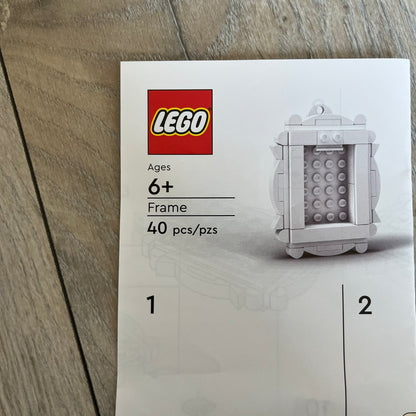 LEGO White Frame Make and Take Build is a limited promotional LEGO set distributed as an exclusive “make & take” event and not available for retail purchase. The model features a fully white 3D frame styled like a picture frame, designed for use as a photo holder. The back includes a hole for hanging or display.