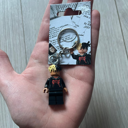 Lego XXXTentacion “XXXBlocktentacion” keychain featuring a custom Lego figure of XXXTentacion in a black/red revenge hoodie, with his classic split black and beige dreads in 3D. The figure is attached to a Lego-style recreation of the 2017 '17' album cover, reimagined in brick graphics. A great tribute and a creative collectible that merges music culture with fan-made Lego artistry, made by TheCanvasDon.