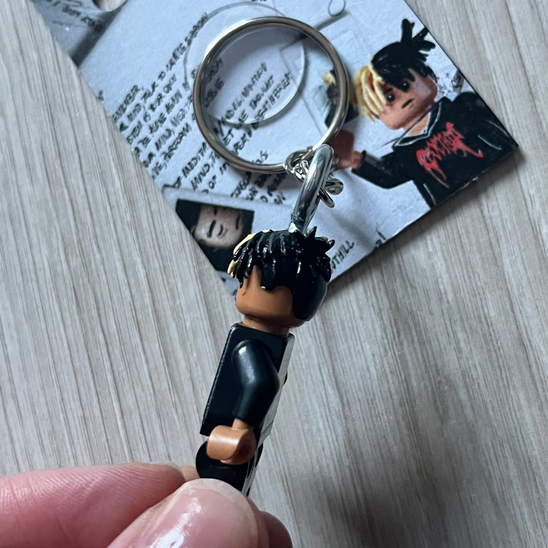 Lego XXXTentacion “XXXBlocktentacion” keychain featuring a custom Lego figure of XXXTentacion in a black/red revenge hoodie, with his classic split black and beige dreads in 3D. The figure is attached to a Lego-style recreation of the 2017 '17' album cover, reimagined in brick graphics. A great tribute and a creative collectible that merges music culture with fan-made Lego artistry, made by TheCanvasDon.