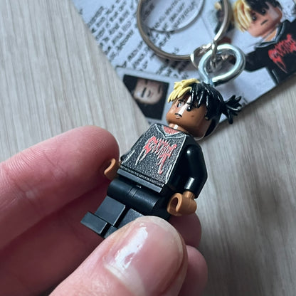 Lego XXXTentacion “XXXBlocktentacion” keychain featuring a custom Lego figure of XXXTentacion in a black/red revenge hoodie, with his classic split black and beige dreads in 3D. The figure is attached to a Lego-style recreation of the 2017 '17' album cover, reimagined in brick graphics. A great tribute and a creative collectible that merges music culture with fan-made Lego artistry, made by TheCanvasDon.