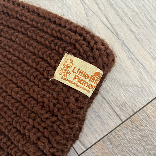 LittleBigPlanet 2009 Europe Exclusive Sackboy Beanie is an officially licensed brown knit beanie made from 100% acrylic. The design is styled after Sackboy and features a beige front tag with an orange Sackboy figure, LittleBigPlanet logo, and SCEE 2009 licensing. This item was released exclusively in the European region. Super rare and rarely seen for sale.