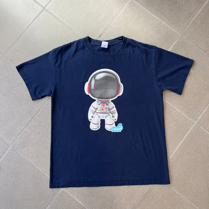 LittleBigPlanet 2011 Astronaut Navy Tee features a navy T-shirt made on a Gildan blank. The front has a white Sackboy graphic wearing an astronaut suit with a grey visor, accompanied by a blue LittleBigPlanet logo near the leg.
