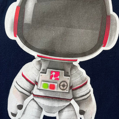 LittleBigPlanet 2011 Astronaut Navy Tee features a navy T-shirt made on a Gildan blank. The front has a white Sackboy graphic wearing an astronaut suit with a grey visor, accompanied by a blue LittleBigPlanet logo near the leg.
