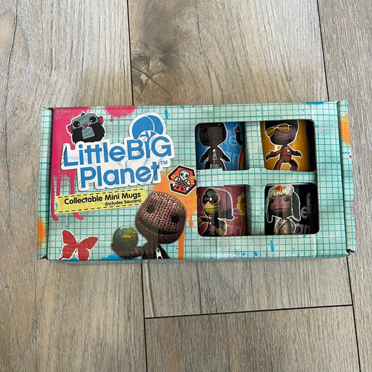 LittleBigPlanet 2011 Collectable Mini Mugs + Saucers Set is a 4-piece espresso set featuring characters from the LittleBigPlanet series, including Sackboy, Marvin the Disco Dancer, Gloria, and Yuri Army Sackboy. Each mini mug includes a wraparound character graphic with the LittleBigPlanet logo and comes with a matching saucer printed on the top. The set is officially licensed by Sony Computer Entertainment, includes a display box, and carries SCEE 2011 licensing on the base of the mugs and saucers.