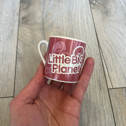 LittleBigPlanet 2011 Collectable Mini Mugs + Saucers Set is a 4-piece espresso set featuring characters from the LittleBigPlanet series, including Sackboy, Marvin the Disco Dancer, Gloria, and Yuri Army Sackboy. Each mini mug includes a wraparound character graphic with the LittleBigPlanet logo and comes with a matching saucer printed on the top. The set is officially licensed by Sony Computer Entertainment, includes a display box, and carries SCEE 2011 licensing on the base of the mugs and saucers.