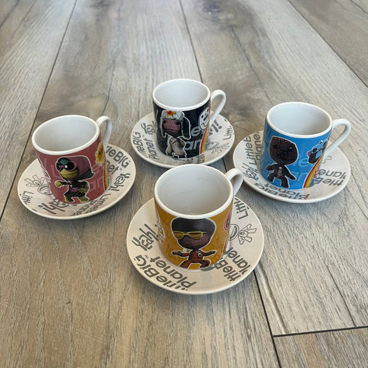 LittleBigPlanet 2011 Collectable Mini Mugs + Saucers Set is a 4-piece espresso set featuring characters from the LittleBigPlanet series, including Sackboy, Marvin the Disco Dancer, Gloria, and Yuri Army Sackboy. Each mini mug includes a wraparound character graphic with the LittleBigPlanet logo and comes with a matching saucer printed on the top. The set is officially licensed by Sony Computer Entertainment, includes a display box, and carries SCEE 2011 licensing on the base of the mugs and saucers.