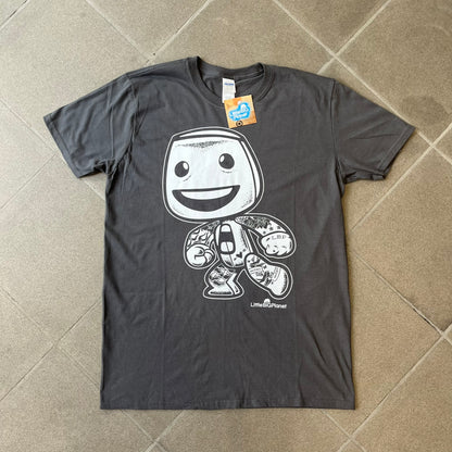 LittleBigPlanet 2016 Tattoo Sackboy Tee features a grey T-shirt made on a Gildan blank. The front has a large white graphic of a running Sackboy covered in tattoo designs, with a LittleBigPlanet logo underneath. Includes the original paper LittleBigPlanet tag.
