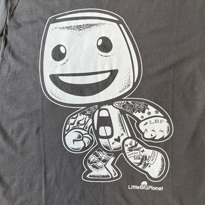 LittleBigPlanet 2016 Tattoo Sackboy Tee features a grey T-shirt made on a Gildan blank. The front has a large white graphic of a running Sackboy covered in tattoo designs, with a LittleBigPlanet logo underneath. Includes the original paper LittleBigPlanet tag.
