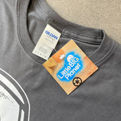 LittleBigPlanet 2016 Tattoo Sackboy Tee features a grey T-shirt made on a Gildan blank. The front has a large white graphic of a running Sackboy covered in tattoo designs, with a LittleBigPlanet logo underneath. Includes the original paper LittleBigPlanet tag.

