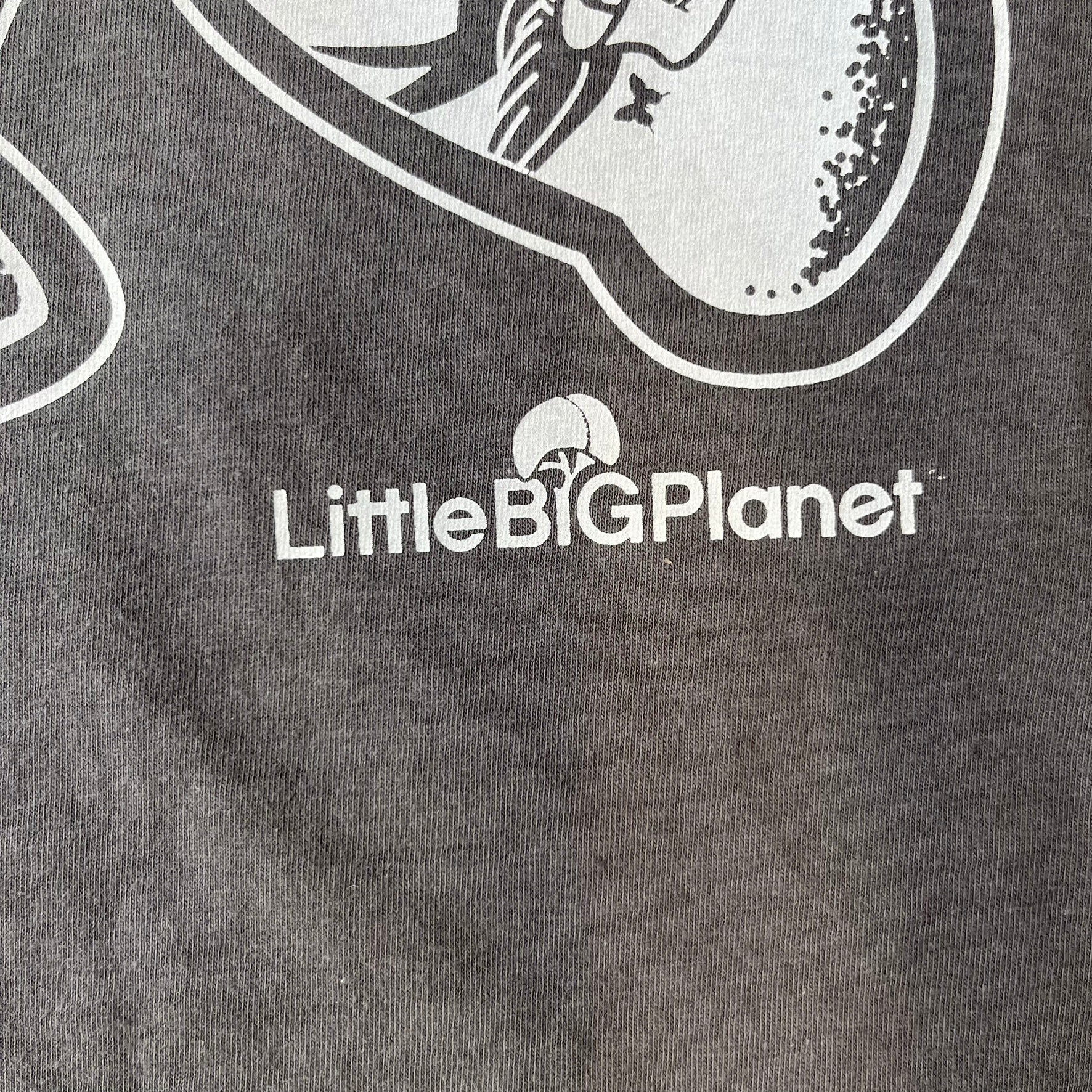 LittleBigPlanet 2016 Tattoo Sackboy Tee features a grey T-shirt made on a Gildan blank. The front has a large white graphic of a running Sackboy covered in tattoo designs, with a LittleBigPlanet logo underneath. Includes the original paper LittleBigPlanet tag.
