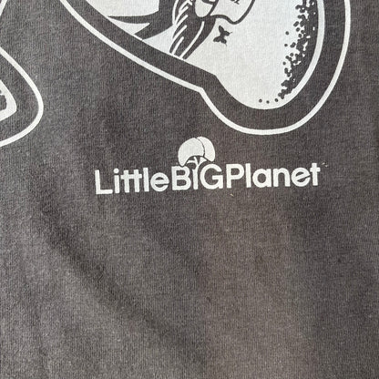 LittleBigPlanet 2016 Tattoo Sackboy Tee features a grey T-shirt made on a Gildan blank. The front has a large white graphic of a running Sackboy covered in tattoo designs, with a LittleBigPlanet logo underneath. Includes the original paper LittleBigPlanet tag.
