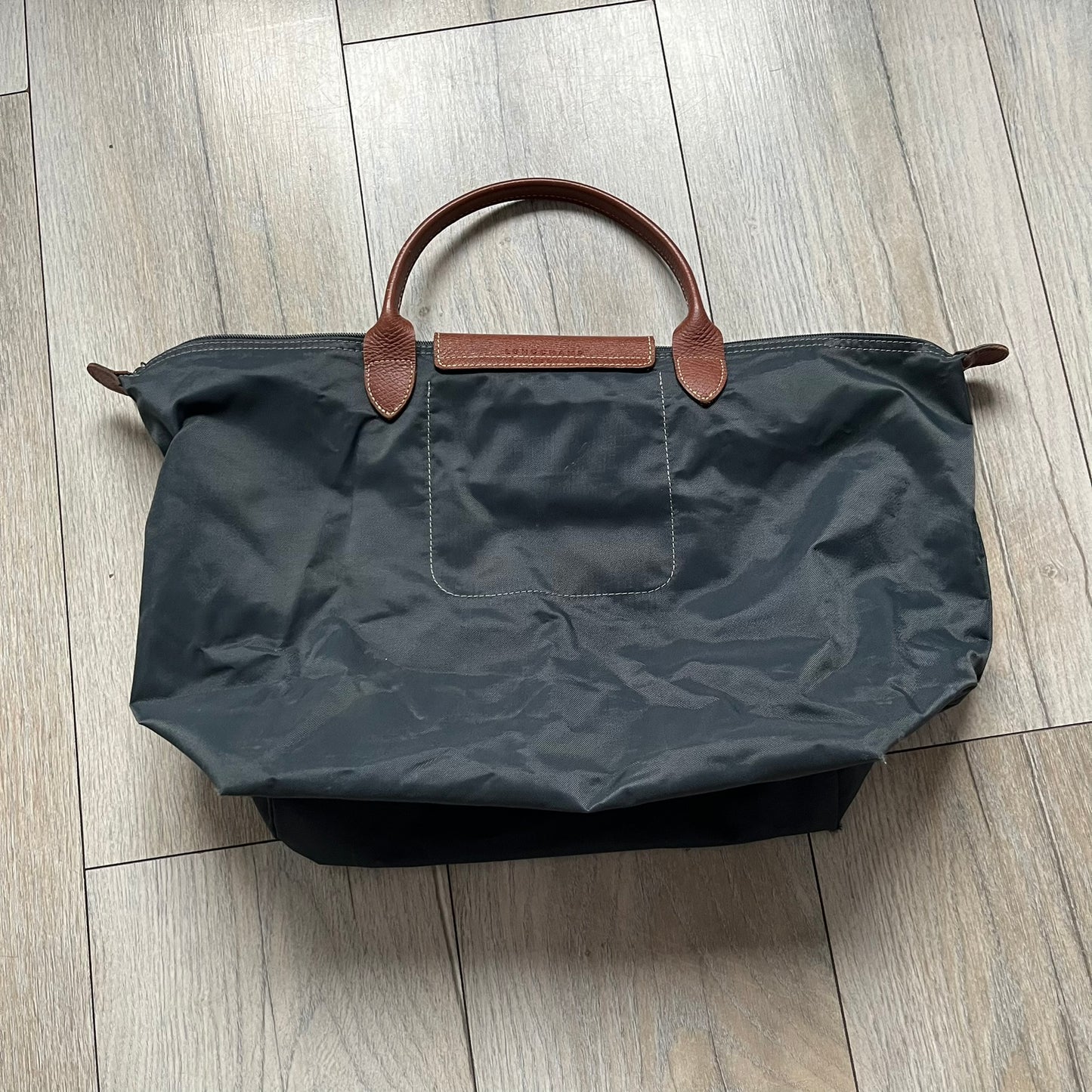 Longchamp x Jeremy Scott 2009 “Medals” Le Pliage Large Handbag is a grey nylon foldable tote with brown leather handles and flap, featuring a branded metal zipper and an interior Jeremy Scott x Longchamp leather tag, made in France. The front showcases embroidered medal motifs, including a Jeremy Scott portrait, Longchamp logo, and key emblem, with one medal designed as a movable attachment. This design is part of the A/W 2009 Military-inspired Colonel line collaboration.