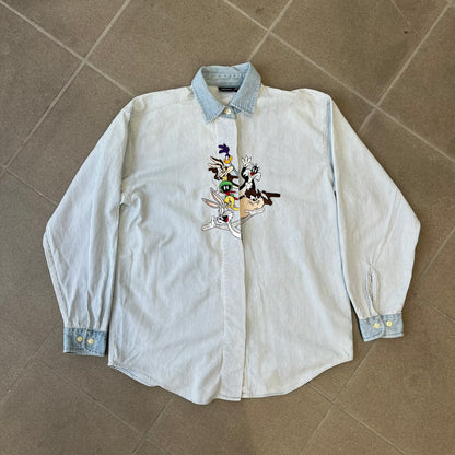 Looney Tunes 1996 Embroidered Striped Shirt features a light blue striped 100% cotton construction with a denim collar and matching denim hems. The center has a colorful embroidered design featuring the Looney Tunes characters Marsian, Bugs Bunny, Taz, Tweety, Sylvester, Road Runner, and Wile E. Coyote appearing from the middle. Made in Hong Kong and finished with a 1996 black licensed neck tag.