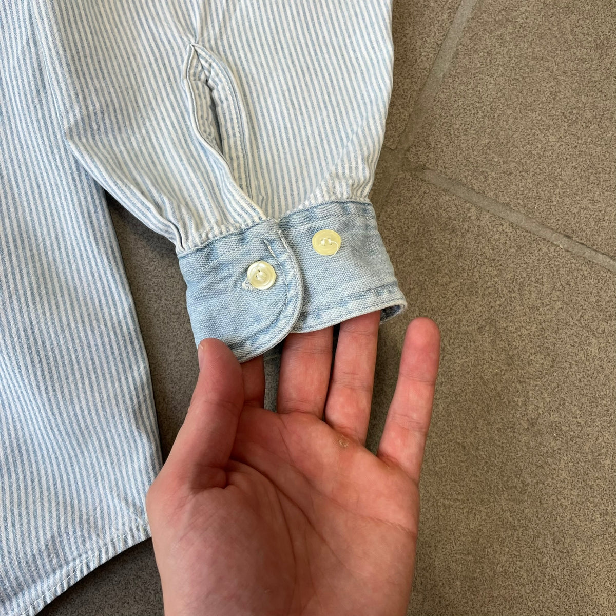 Looney Tunes 1996 Embroidered Striped Shirt features a light blue striped 100% cotton construction with a denim collar and matching denim hems. The center has a colorful embroidered design featuring the Looney Tunes characters Marsian, Bugs Bunny, Taz, Tweety, Sylvester, Road Runner, and Wile E. Coyote appearing from the middle. Made in Hong Kong and finished with a 1996 black licensed neck tag.