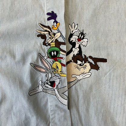 Looney Tunes 1996 Embroidered Striped Shirt features a light blue striped 100% cotton construction with a denim collar and matching denim hems. The center has a colorful embroidered design featuring the Looney Tunes characters Marsian, Bugs Bunny, Taz, Tweety, Sylvester, Road Runner, and Wile E. Coyote appearing from the middle. Made in Hong Kong and finished with a 1996 black licensed neck tag.
