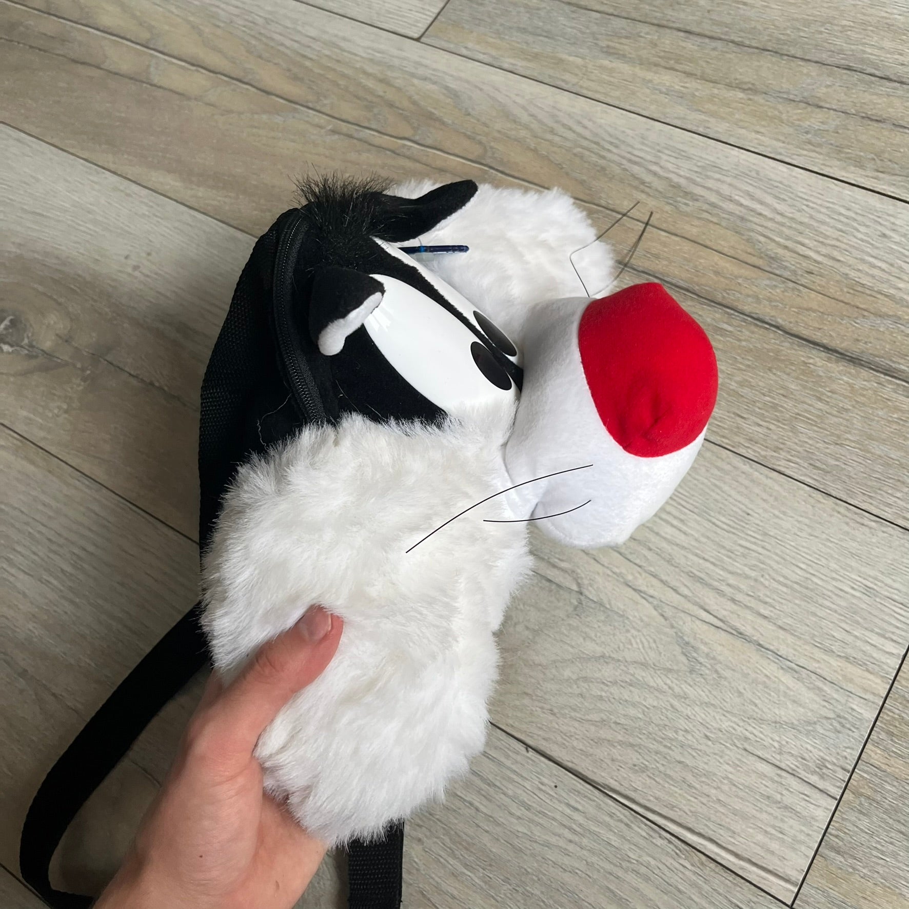 Looney Tunes 1996 Sylvester Head Backpack is a backpack shaped like Sylvester’s head. It features a furry exterior, white plastic eyes, a red nose, and detailed character features throughout. The backpack includes black shoulder straps, a blue plastic Warner Bros. tag, and a 1996 licensing tag.