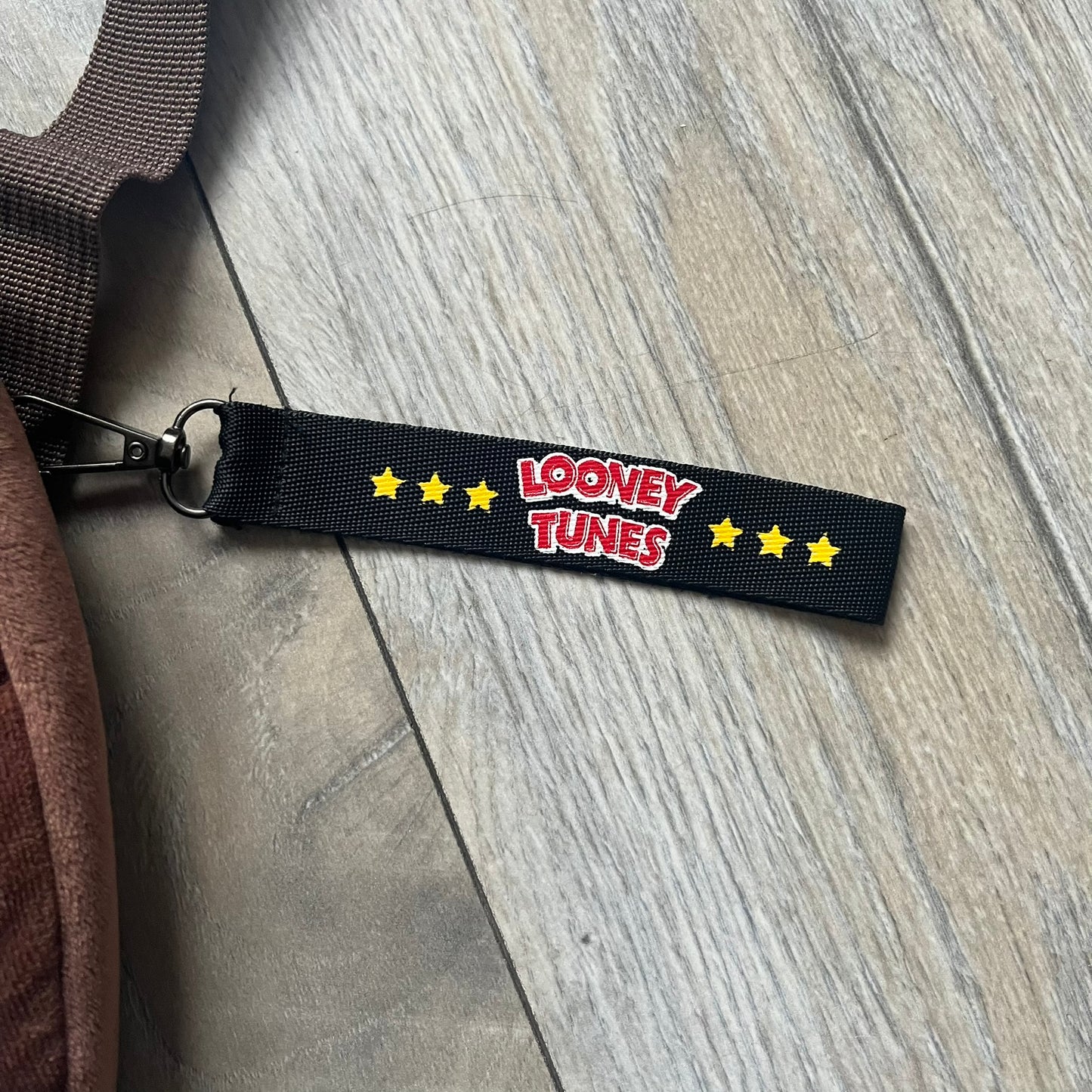 Small plush backpack made from soft brown material, featuring a large 3D Tasmanian Devil face on the front panel. Equipped with a zip closure detailed with a black Looney Tunes branded zipper pull, similar to a keychain tag. Finished with original Looney Tunes tags and compact backpack proportions suitable for light carry.