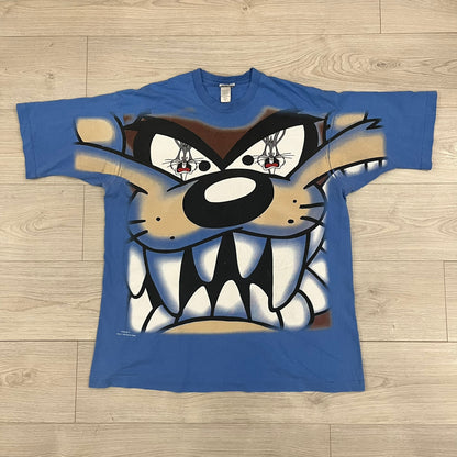 Looney Tunes “Taz & Bugs Bunny” 1997 Freeze Tee featuring a blue base with an all-over front print. The graphic shows Taz with an angry expression and Bugs Bunny reflected in his eyes, with 1997 Warner Bros. Freeze licensing printed below. Made in the USA from 100% cotton.