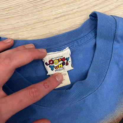 Looney Tunes “Taz & Bugs Bunny” 1997 Freeze Tee featuring a blue base with an all-over front print. The graphic shows Taz with an angry expression and Bugs Bunny reflected in his eyes, with 1997 Warner Bros. Freeze licensing printed below. Made in the USA from 100% cotton.