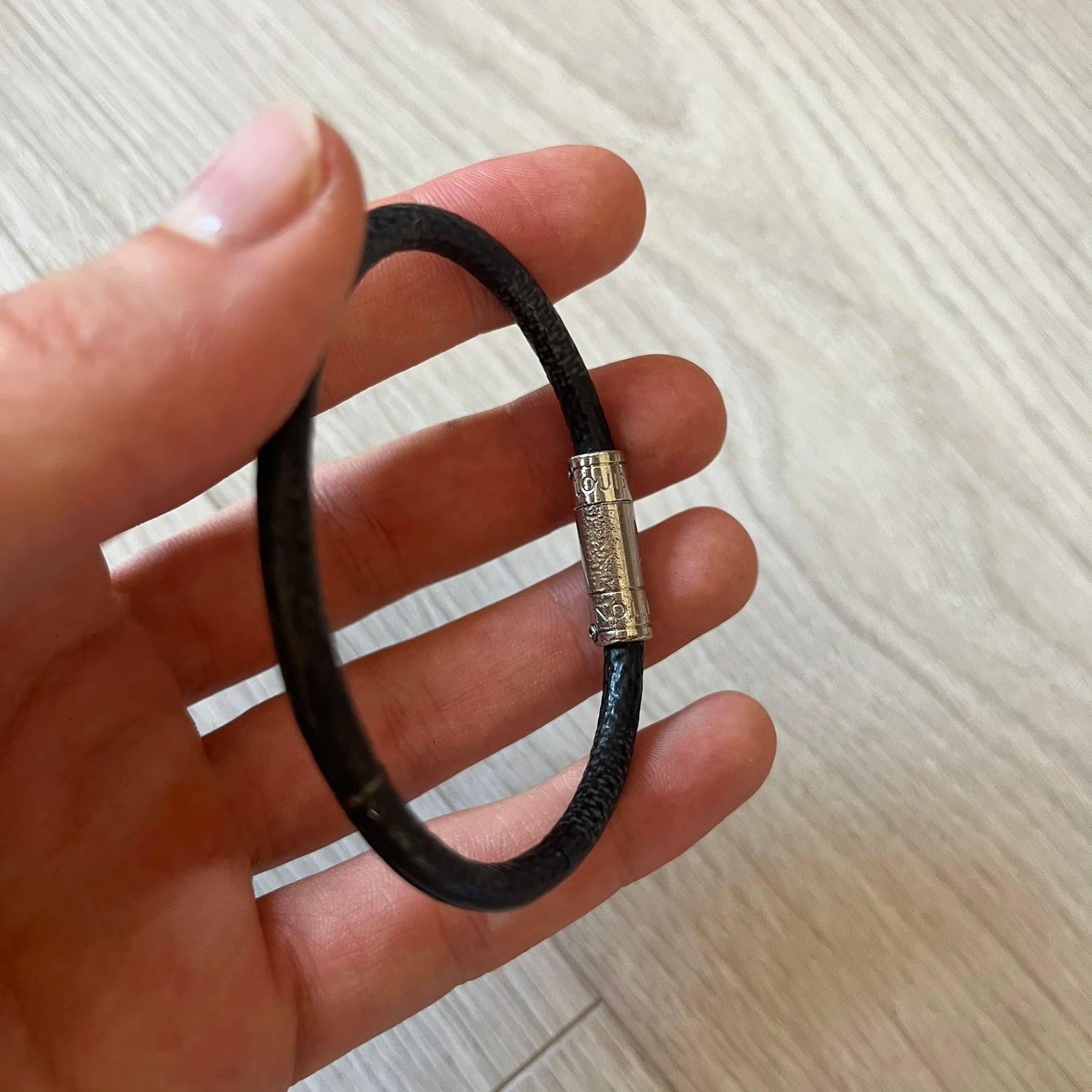 Black leather bracelet with a silver clasp held in a hand on a light wooden surface