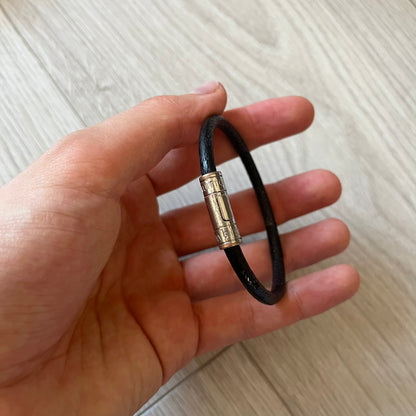 Black leather bracelet with a gold clasp held in a hand on a light wooden surface