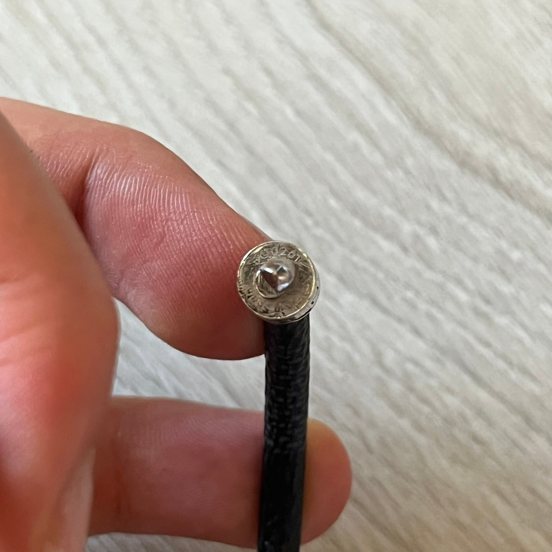Hand holding a black cord with a metallic connector against a white background