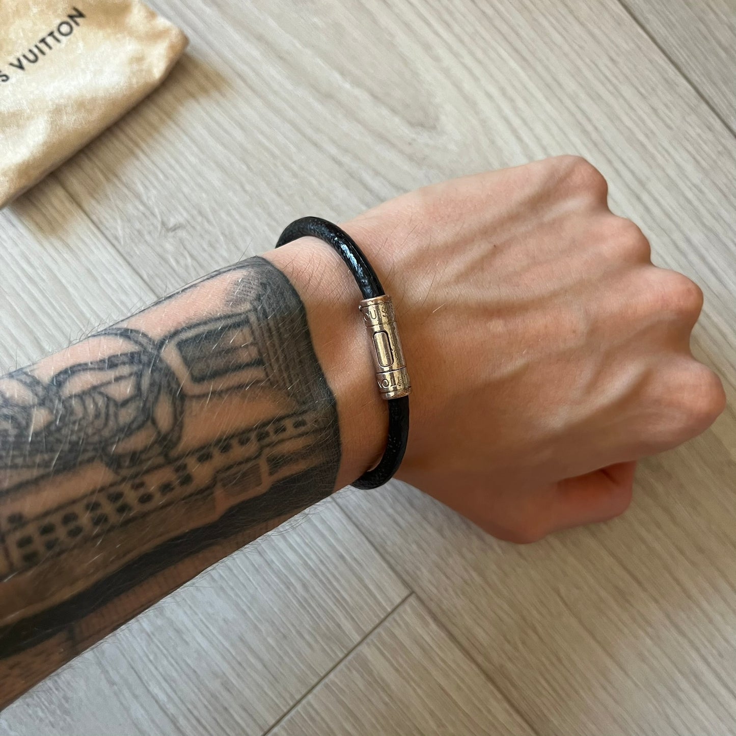 Person wearing a black bracelet with a gold clasp on a wooden surface