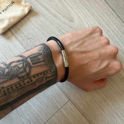 Person wearing a black bracelet with a gold clasp on a wooden surface