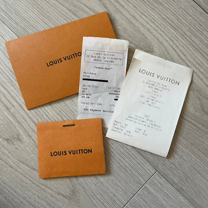 Louis Vuitton documents including a brown paper bag, receipt, and card on a gray surface