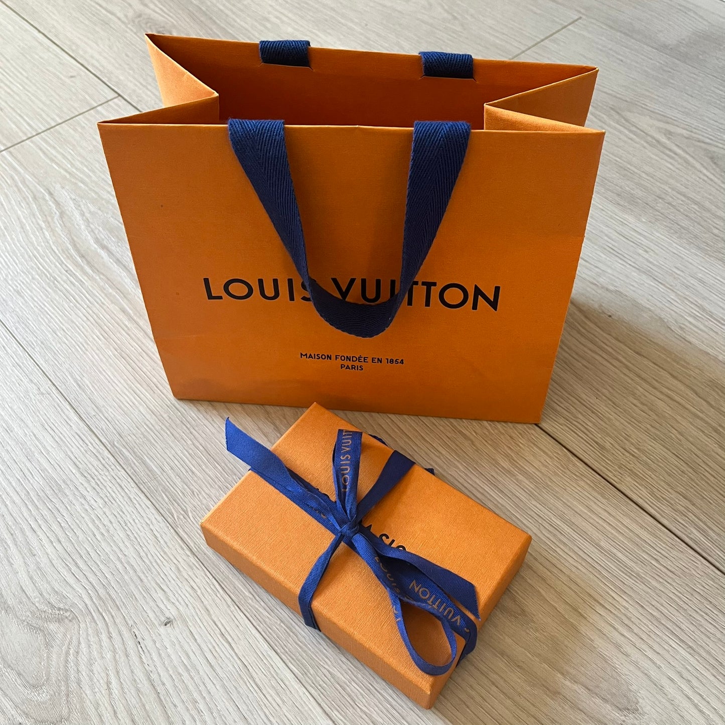 Louis Vuitton shopping bag and gift box with blue ribbon on a wooden surface