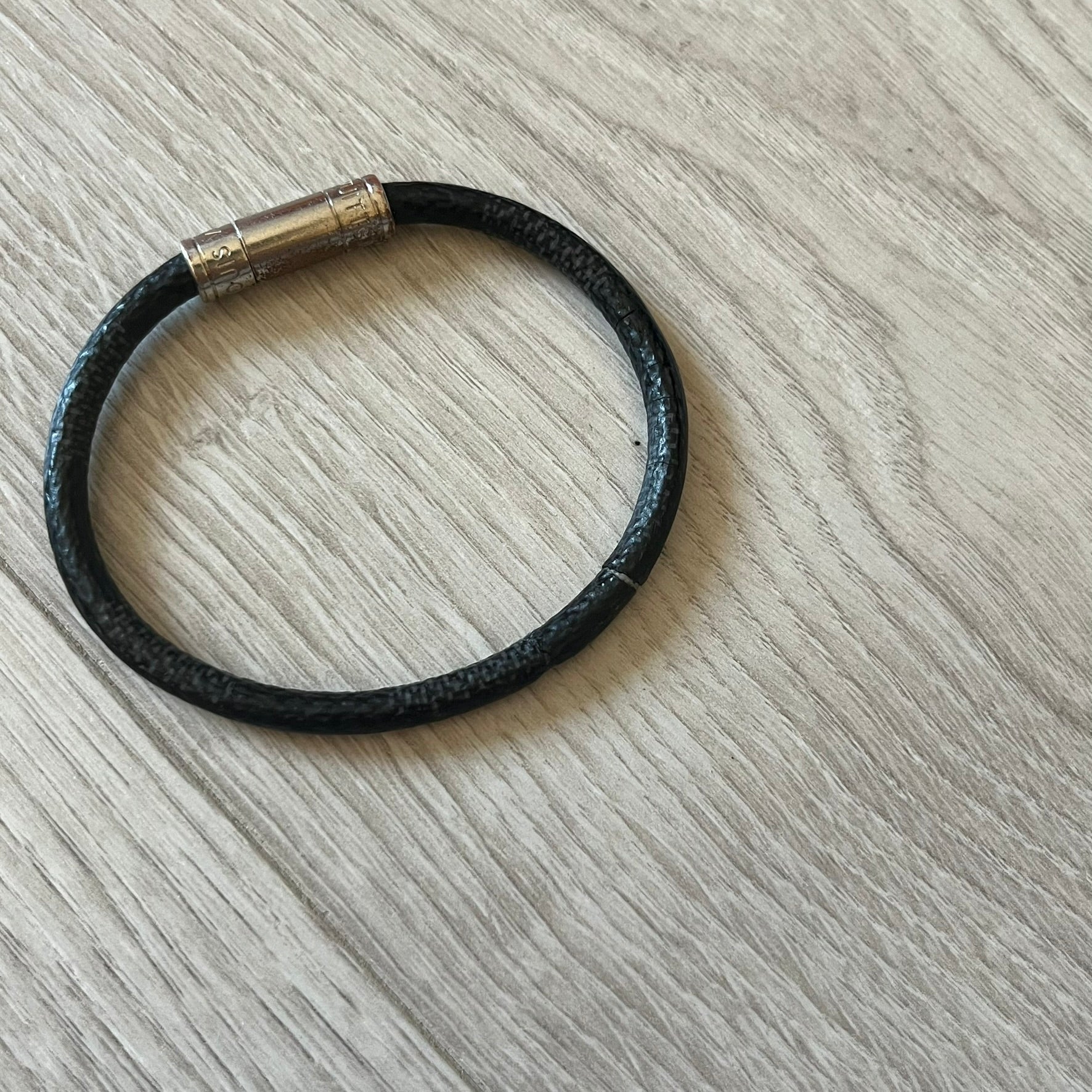Black leather bracelet with a metallic clasp on a light wooden surface