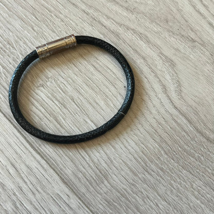 Black leather bracelet with a metallic clasp on a light wooden surface
