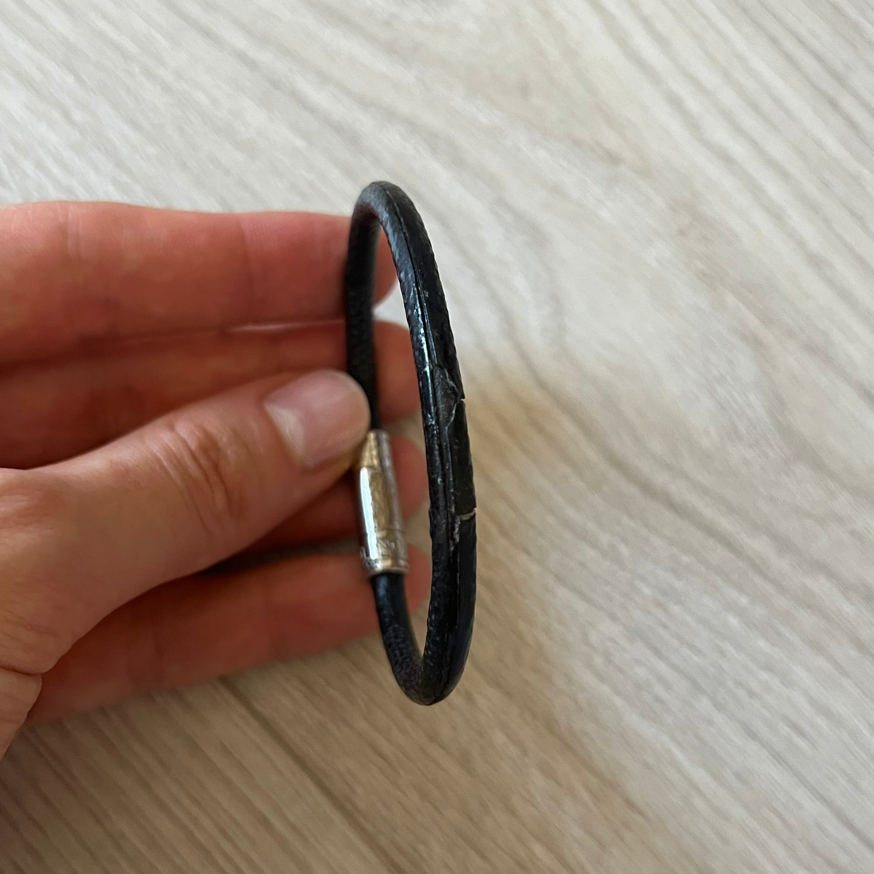 Black leather bracelet held in a hand on a light wooden surface