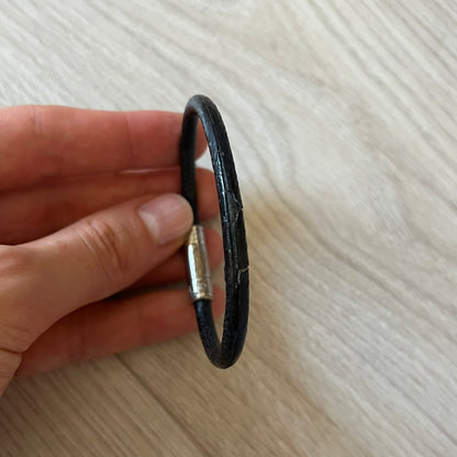 Black leather bracelet held in a hand on a light wooden surface