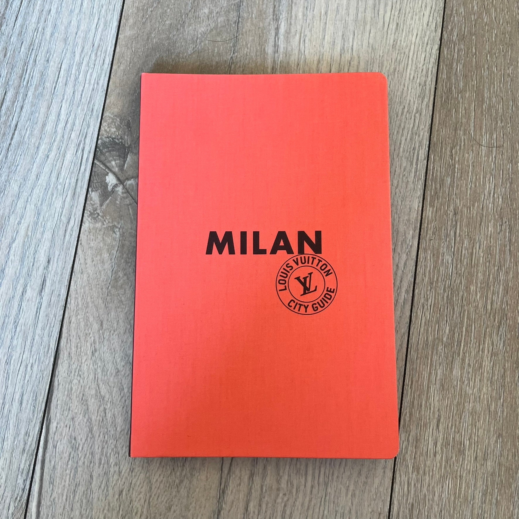 Louis Vuitton *Milan* City Guide is an English-language travel guide with a cloth-bound hardcover. It features recommendations for hotels, restaurants, museums, shopping, and cultural attractions throughout Milan. The edition includes guest contributions by Mahmood, writing by Pierre Léonforte, Corrado Beldi, Katia Kulawick-Assante, and Isabelle Valembras Dahirel, along with exclusive photography by Denis Bourges.
